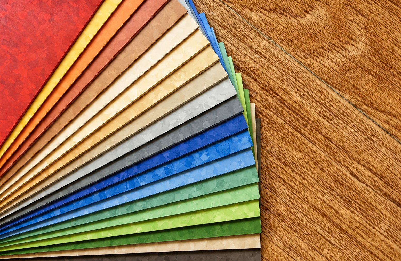 Des échantillons de revêtement de sol vinyle de nombreuses couleurs sont disposés en éventail sur une surface en bois.