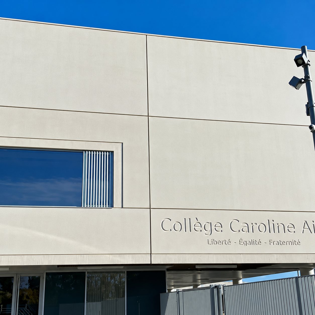 Façade moderne en panneaux de béton clair d'un collège, avec une grande fenêtre et l'inscription de son nom accompagnée de la devise républicaine.