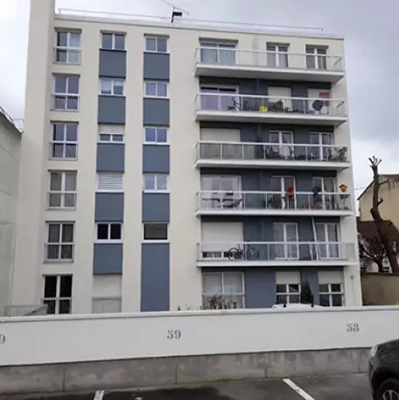 Immeuble d'habitation de six étages à la façade blanche et grise fraîchement rénovée, avec balcons et mur d'enceinte portant les numéros 39 et 38.