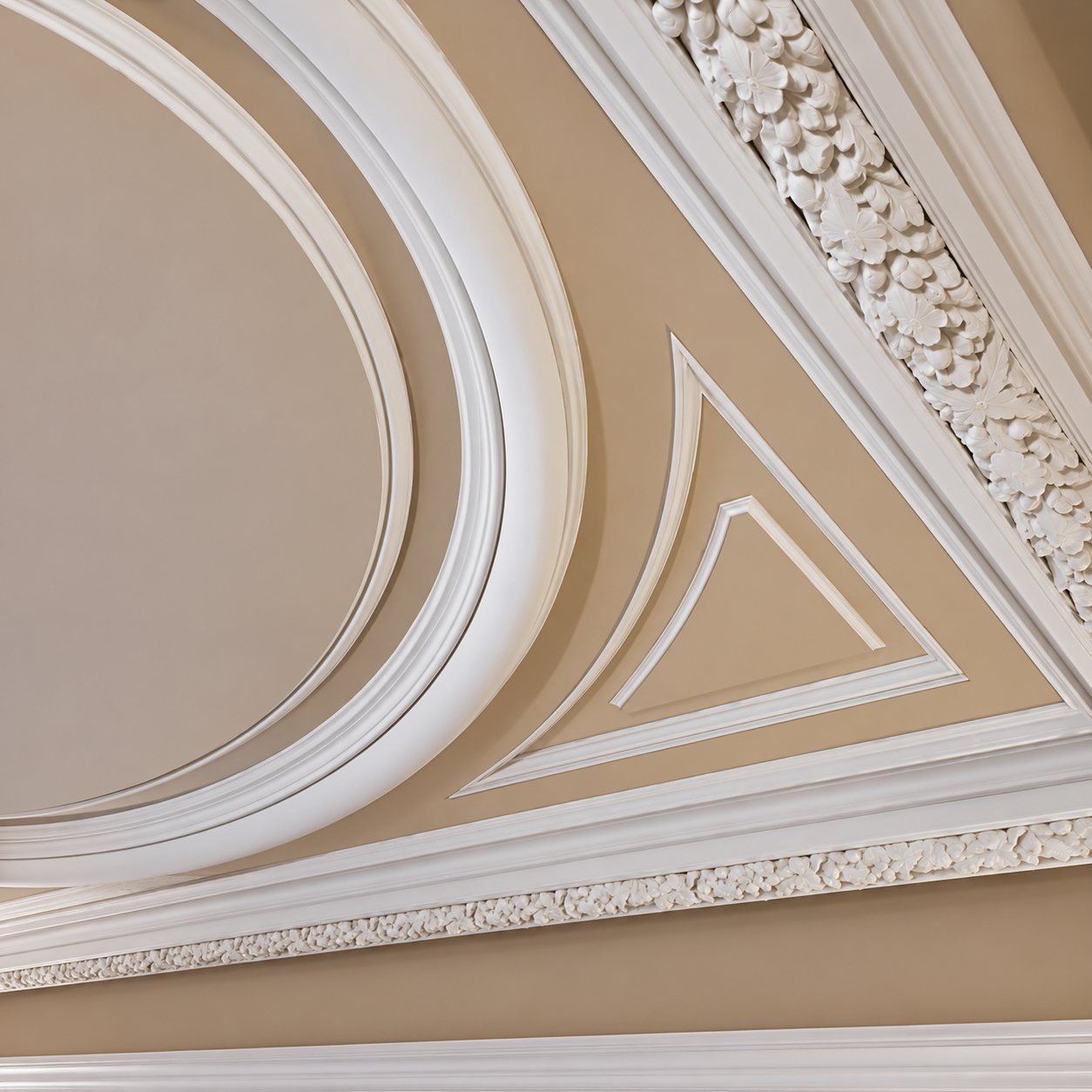 Détail d'un plafond décoré de moulures en plâtre blanches, avec un médaillon ovale, un triangle en relief et une frise sculptée de motifs végétaux sur fond beige.
