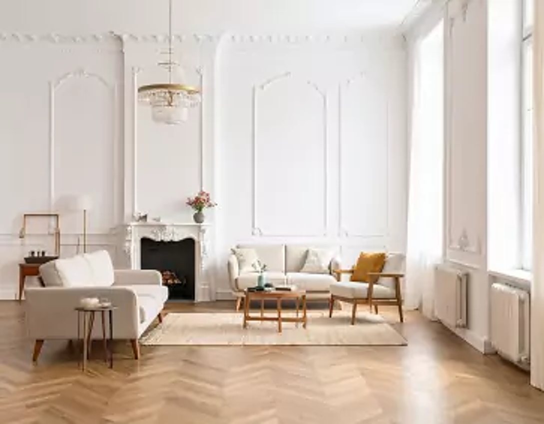 Grand salon lumineux aux murs blancs moulurés, meublé de canapés beiges, d'un fauteuil en bois et d'une table basse sur un parquet en point de Hongrie.